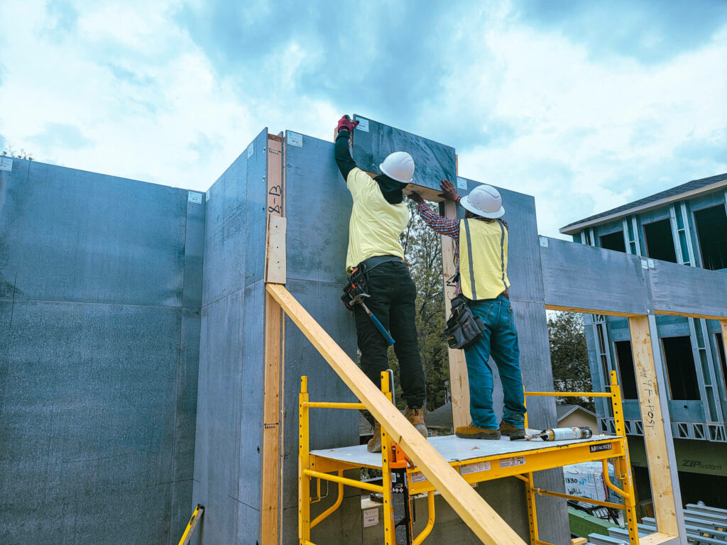Two workers setting a large insulated wall panel into place